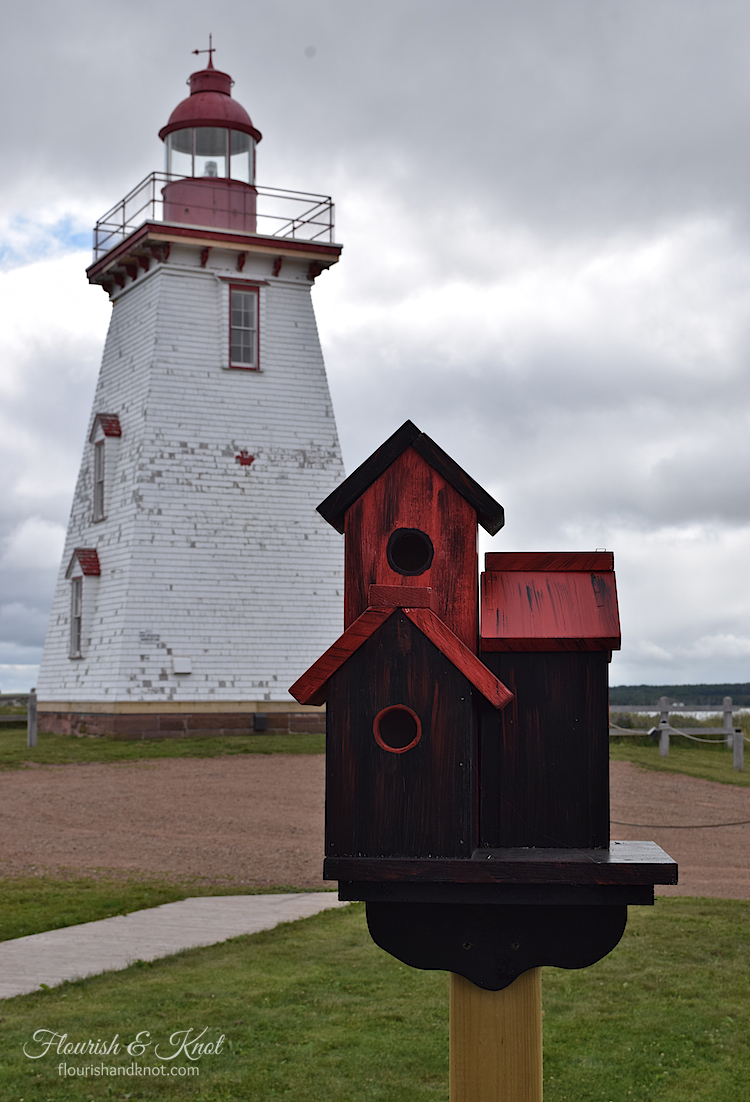 A red birdhouse in front of the historic lighthouse in Souris, PEI