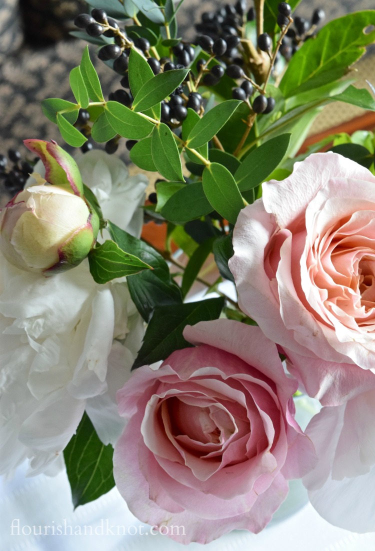 White peonies, peach and pink roses, and dark blue berries in a floral arrangement | flourishandknot.com