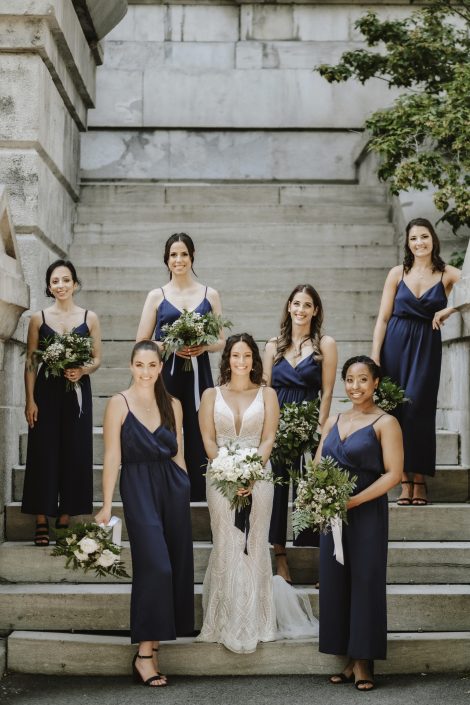 Bride with bridesmaids in navy jumpsuits with white and green bouquets