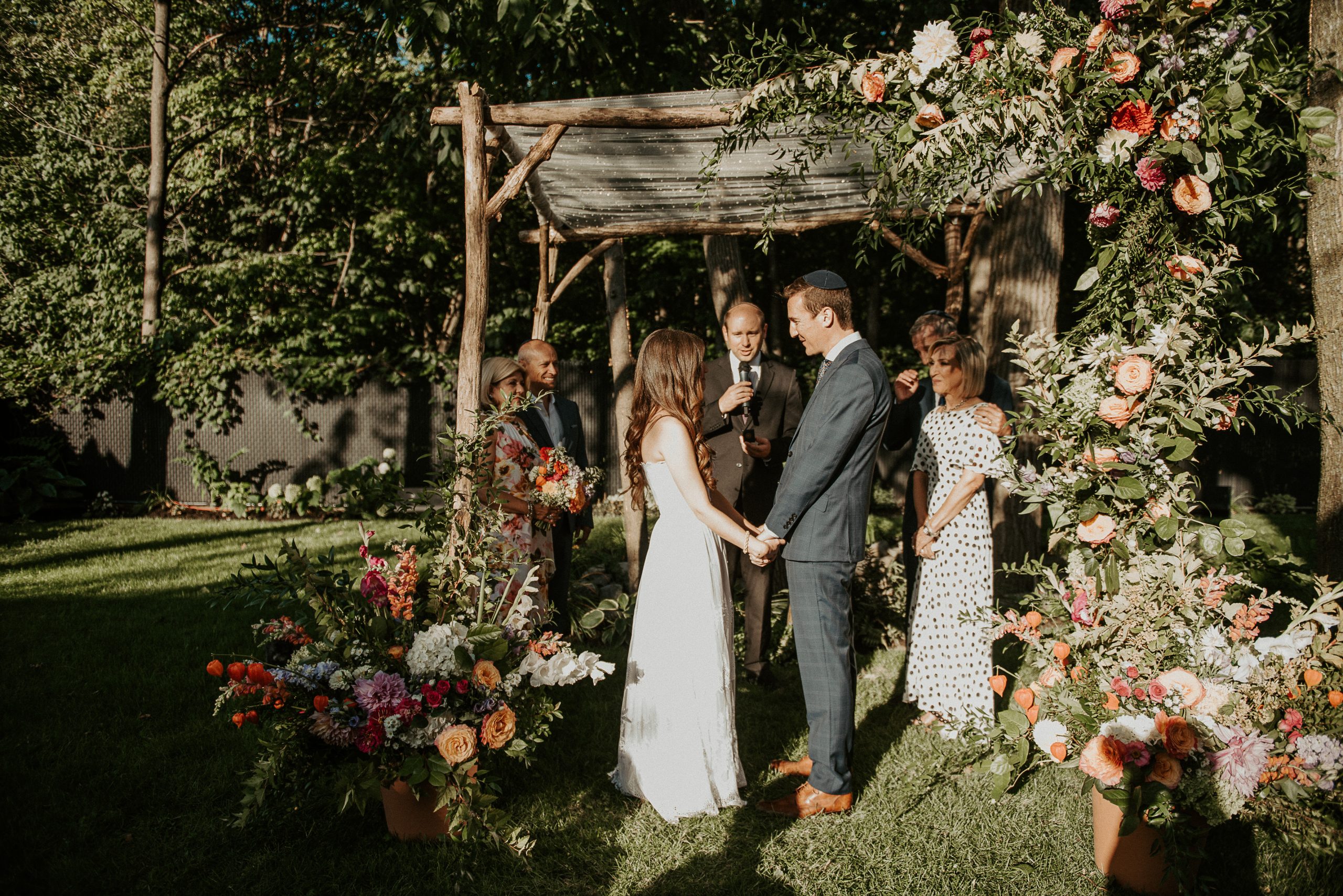 Bride and Groom with family under colourful summer chuppah at outdoor backyard wedding ceremony | L'Orangerie Photographie | Flourish & Knot