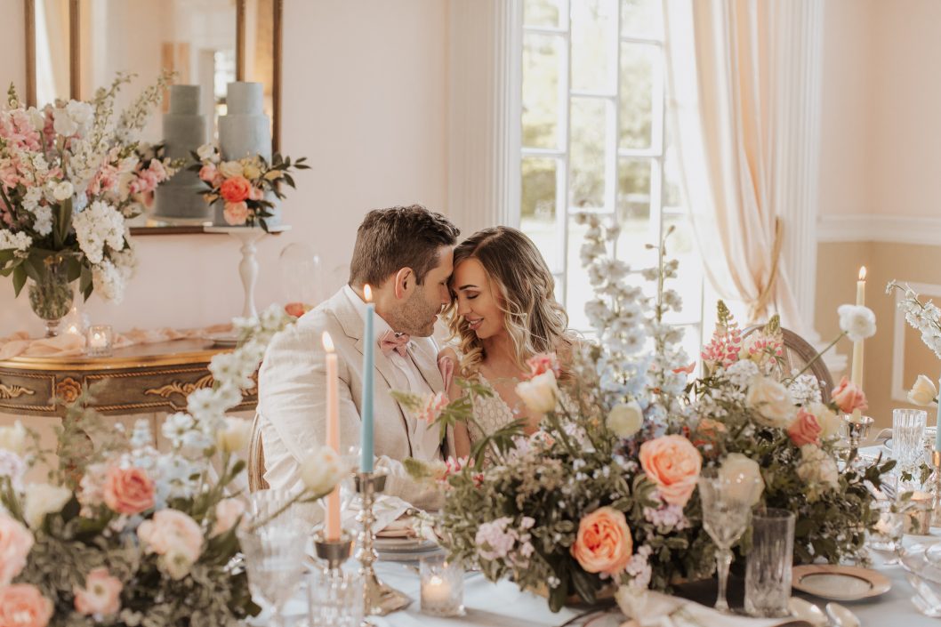 Bride and groom with foreheads together at lush tablescape with peach and blue taper candles and flowers | Kerstin Hahn Photography | Flourish & Knot