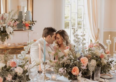 Bride and groom with foreheads together at lush tablescape with peach and blue taper candles and flowers | Kerstin Hahn Photography | Flourish & Knot