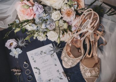 Flat lay of bridal bouquet in peach and pale blue with blush shoes and invitation suite