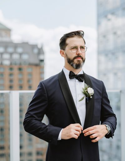 Groom in navy and black suit with classic white and green boutonniere with city in background