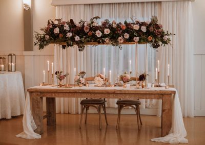 Luxurious floral elevated bridge centrepiece above sweetheart table with bud vases and taper candles | Flourish & Knot