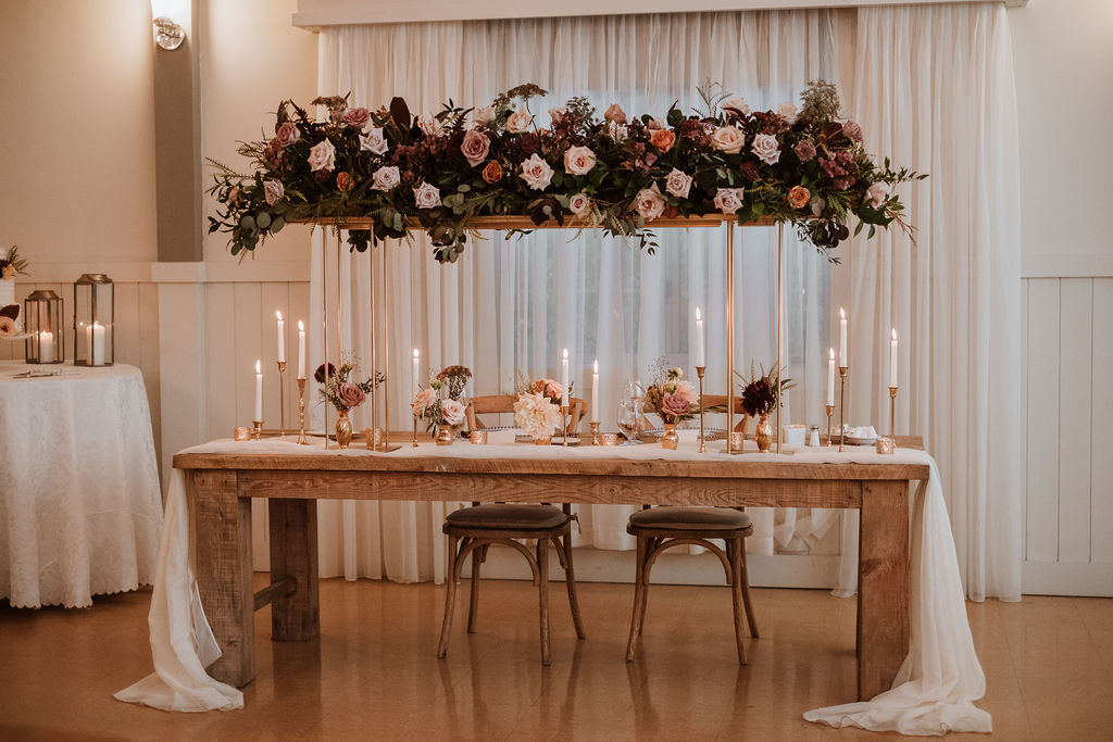 Luxurious floral elevated bridge centrepiece above sweetheart table with bud vases and taper candles | Flourish & Knot