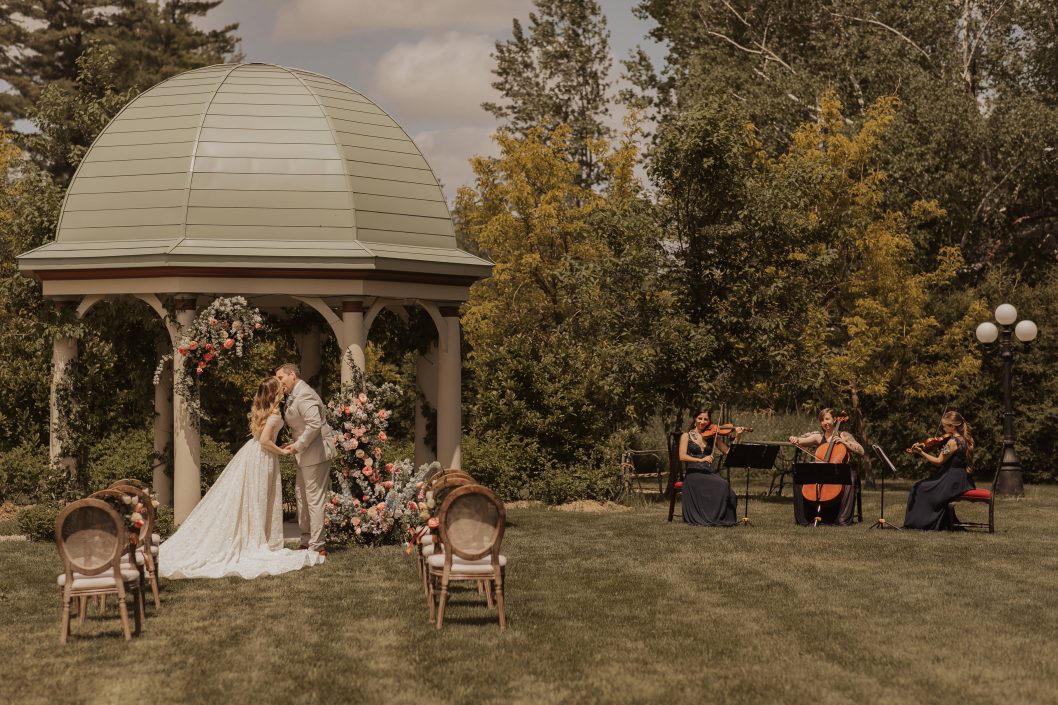 Bride and groom in front of lush wedding ceremony flowers with string trio