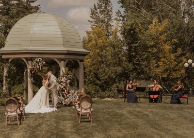 Bride and groom in front of lush wedding ceremony flowers with string trio