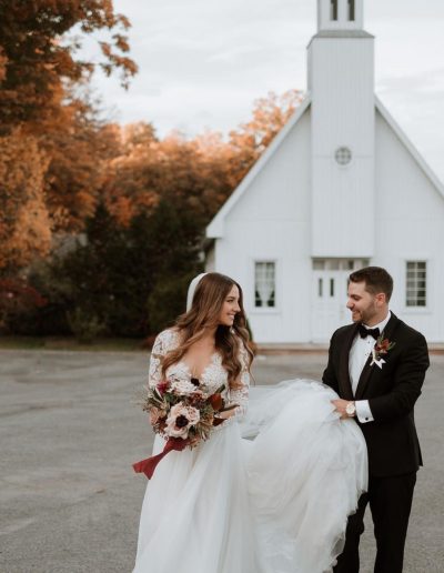 Bride and groom at fall wedding with church in background and autumnal bridal bouquet