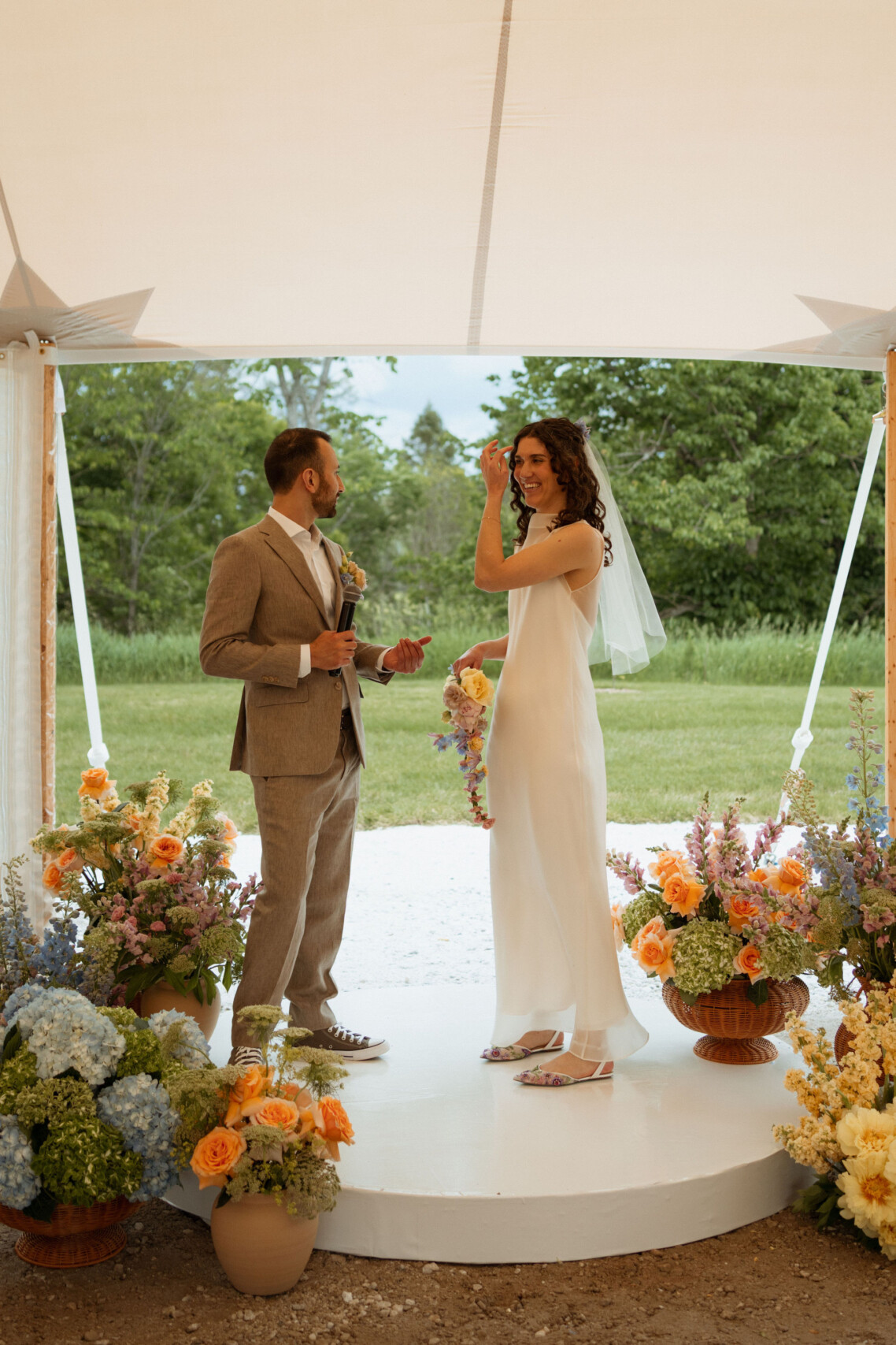 A bride in a minimalist designer gown and a groom exchange vows on a circular white custom wedding stage during an intimate tented wedding at Le Peaches & Cream in the Gatineau Hills.